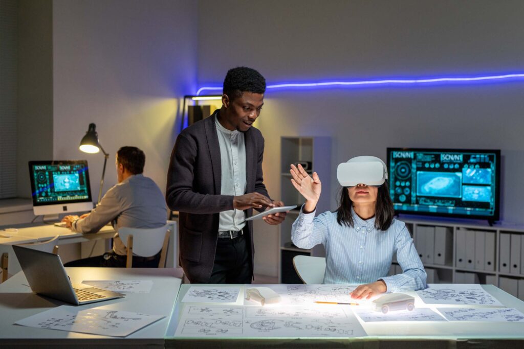 African American employee synchronizing tablet virtual reality headset of Asian colleague while they designing car in 3D