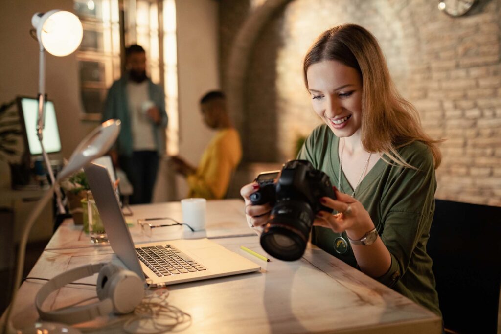 Happy female photographer checking images on digital camera while working at night in a studio.