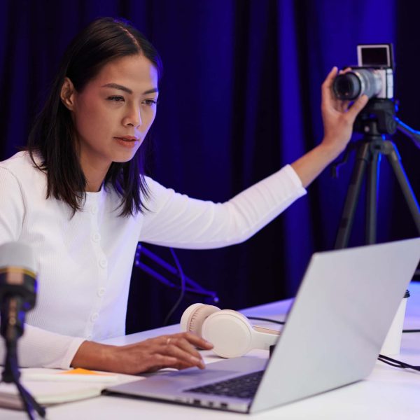 Blogger setting camera and checking picture on laptop before filming video for her channel